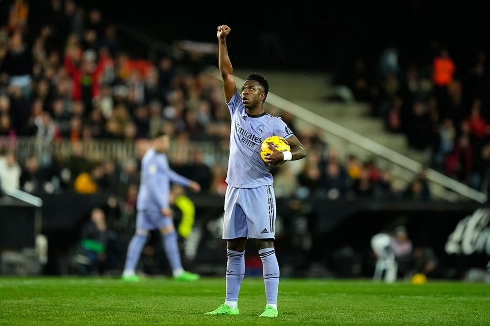 Vinícius Júnior of Real Madrid holds the ball under one arm and raises a fist